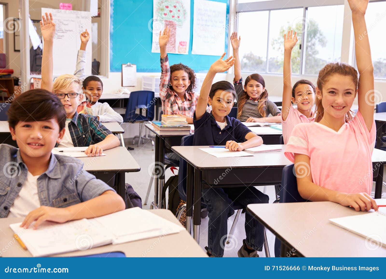 ary school kids in a classroom raising their hands