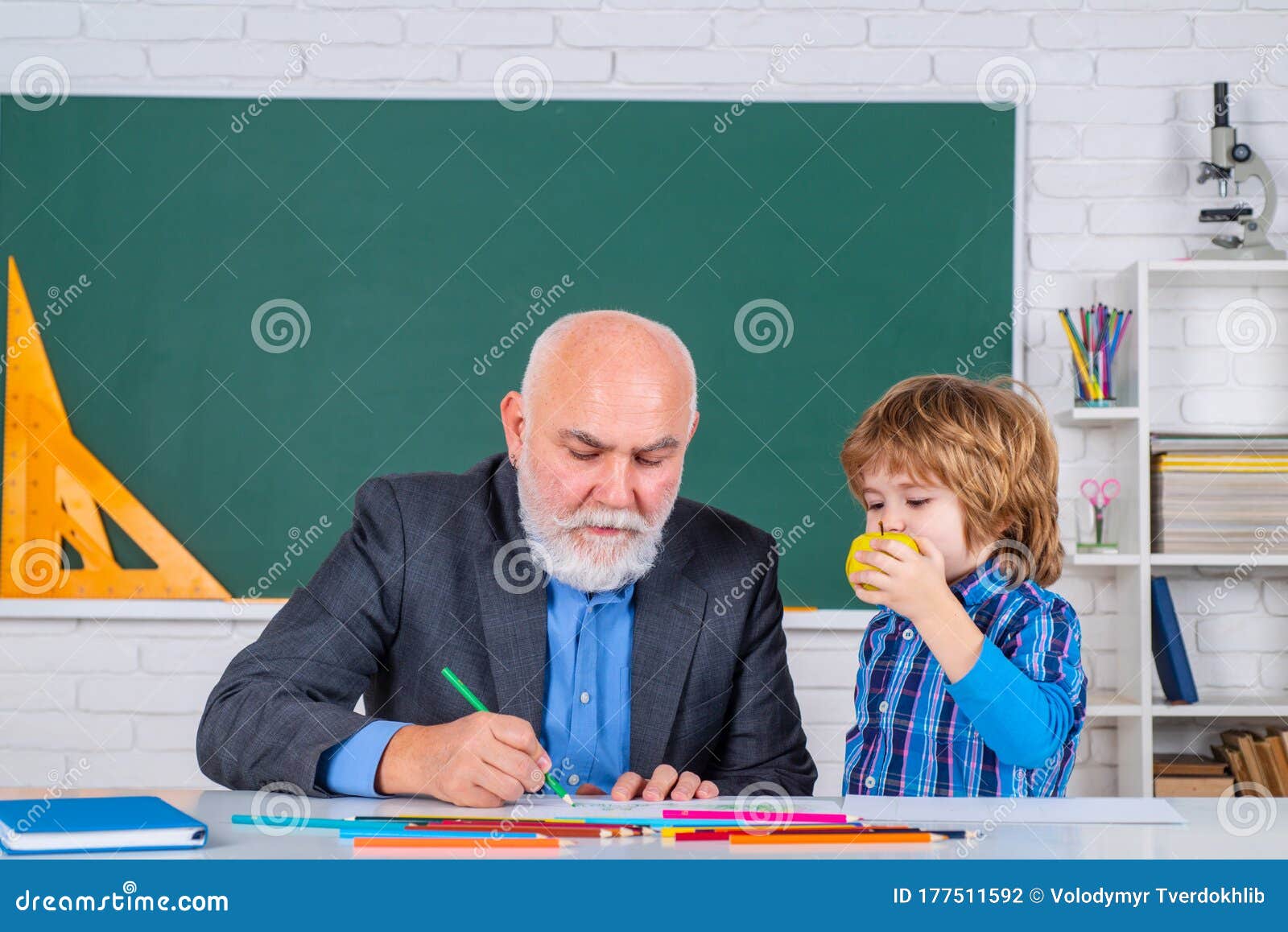 Elementary School Pupil Study At School With Old Teacher