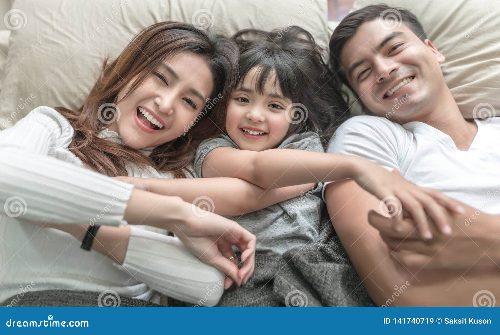 elevated view portrait of happy family lying on bed and looking up and holding hands.