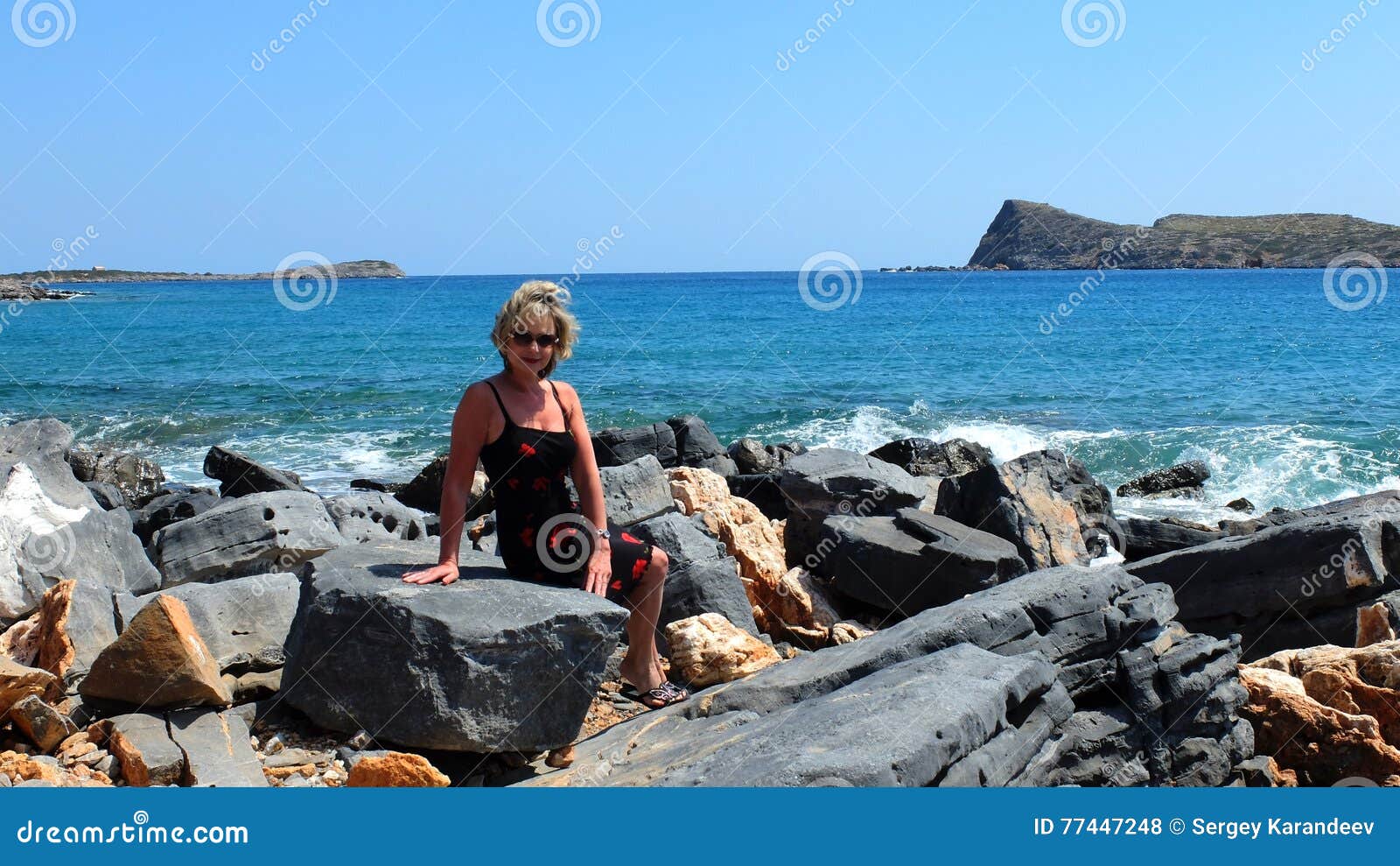 Donna che si siede sulla pietra contro il mare nella città di Elounda, in Creta orientale La Grecia