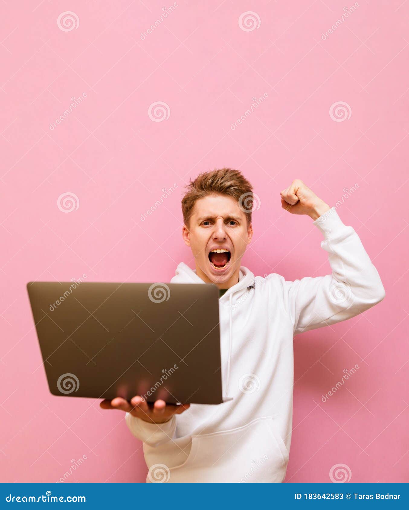 emotional guy rejoices in victory with a laptop in his hands, looks into the camera and shouts with joy, on pink