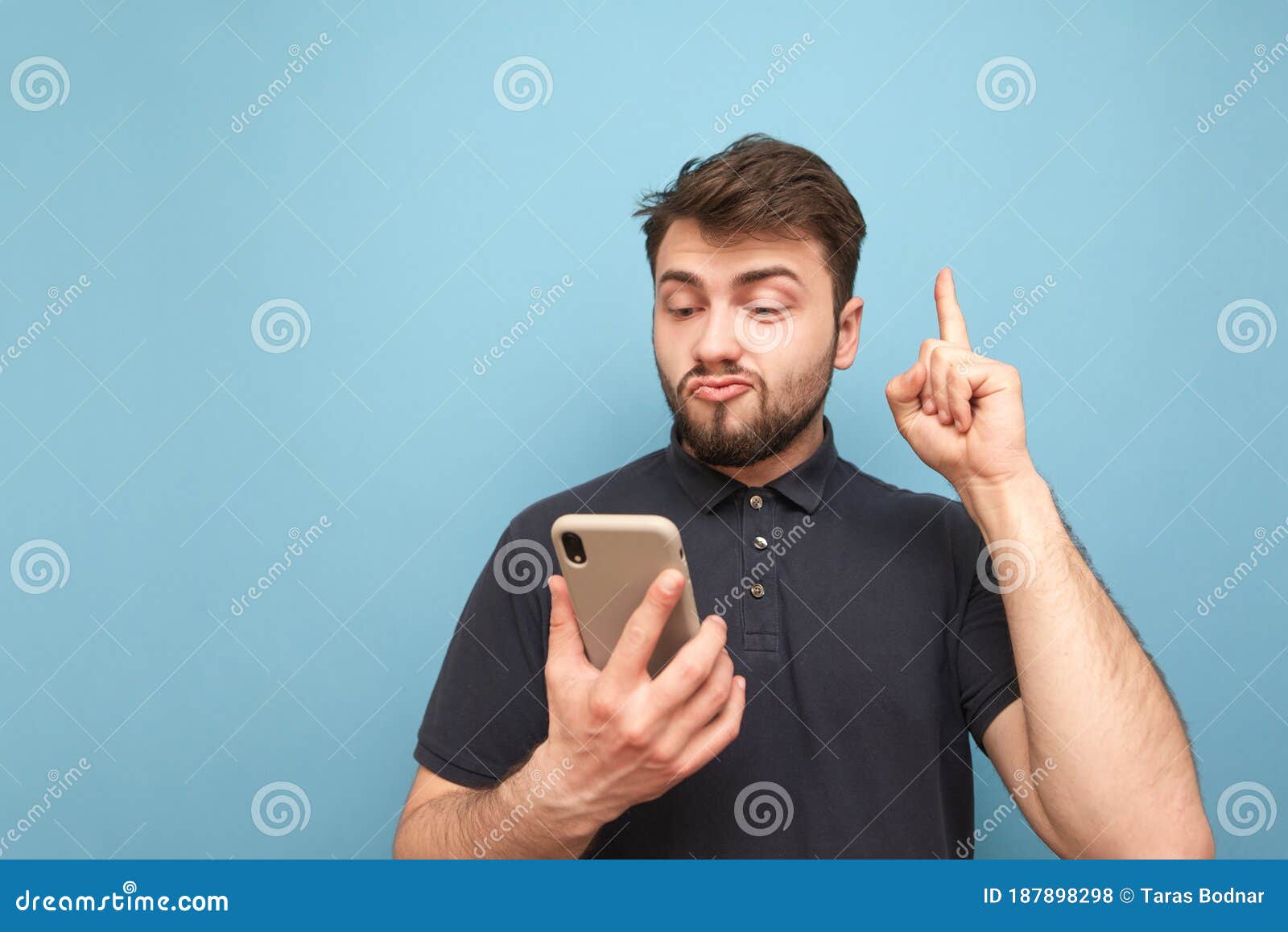 Emotional Man With A Beard Holds A Smartphone In His Hands Showing His Finger Up In A Blank