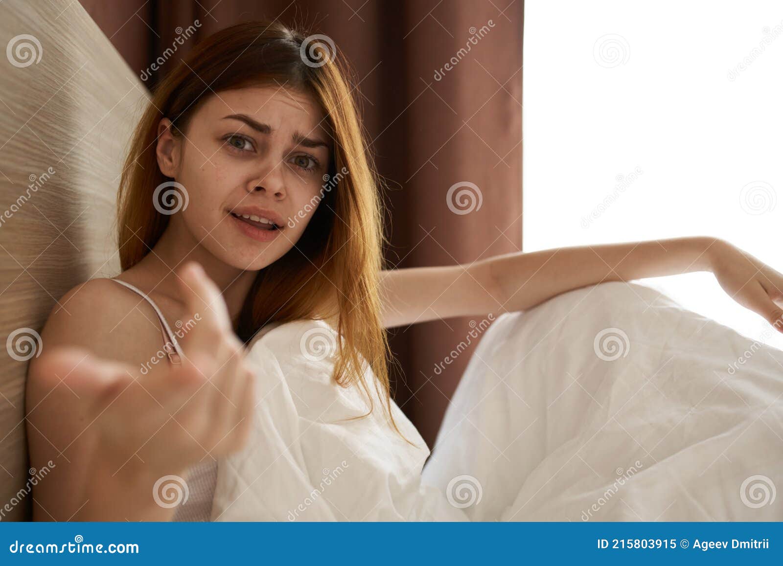 Emotional Woman Lies In Bed Under The Covers And Gestures With Her Hands Near The Copy Space