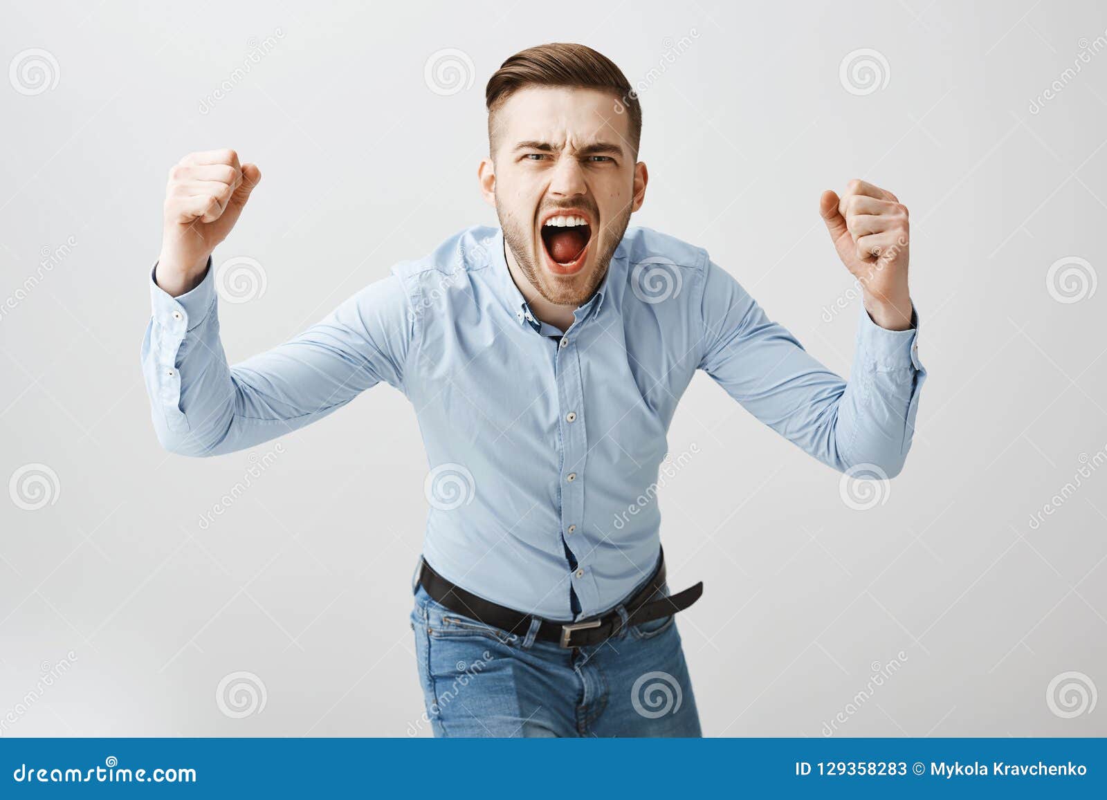 emotive thrilled concerned european male boss in formal blue shirt and jeans bending towards camera yelling and raising