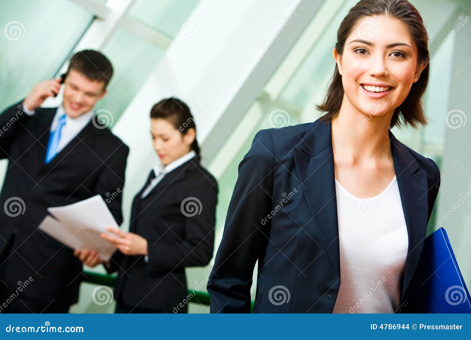 Retrato del empleado alegre en el juego que sostiene la carpeta en el fondo de hombres de negocios