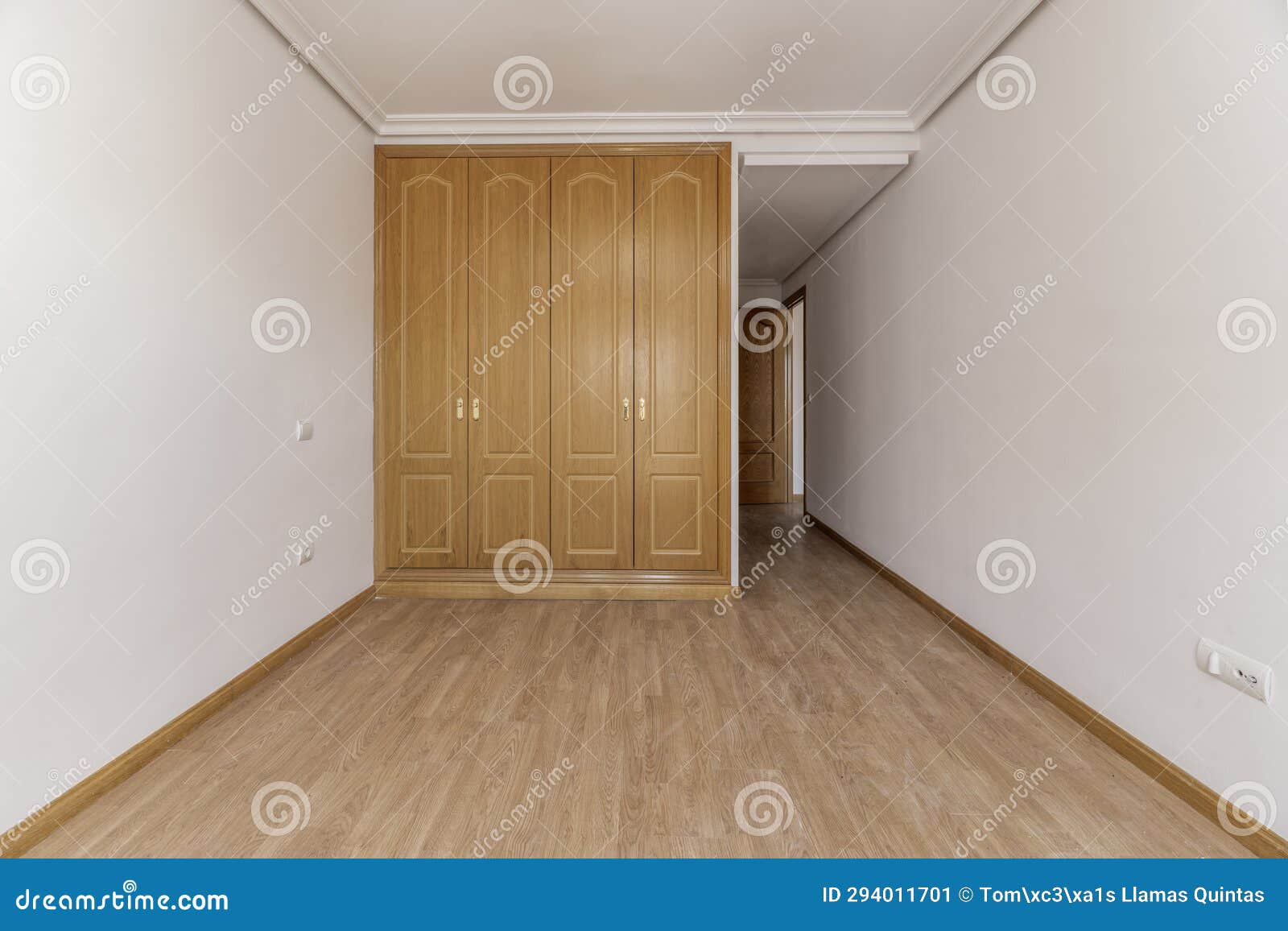 empty bedroom with a built-in three-door oak wardrobe with gold handles, skirting boards of the same material, plain white painted