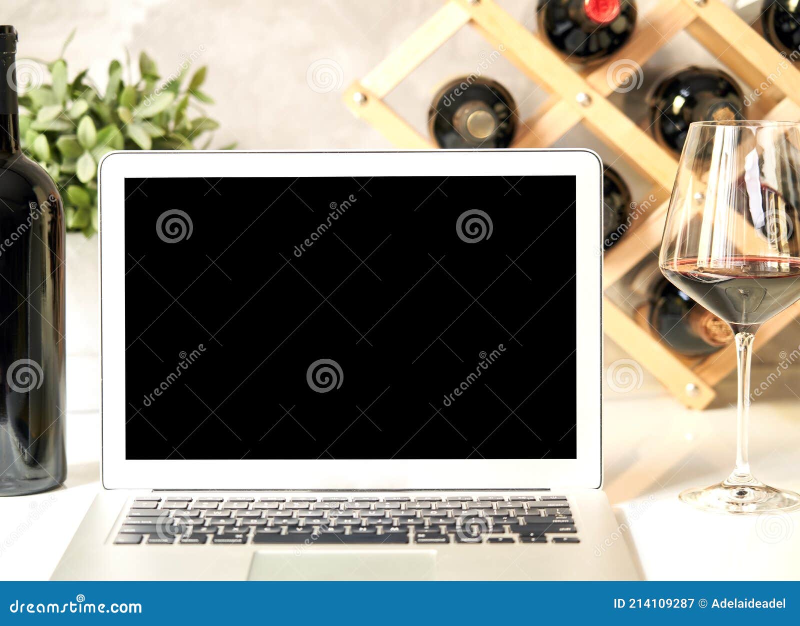 empty blank screen laptop computer on table with wine bottle wine rack holder in the background. buying wines online, home