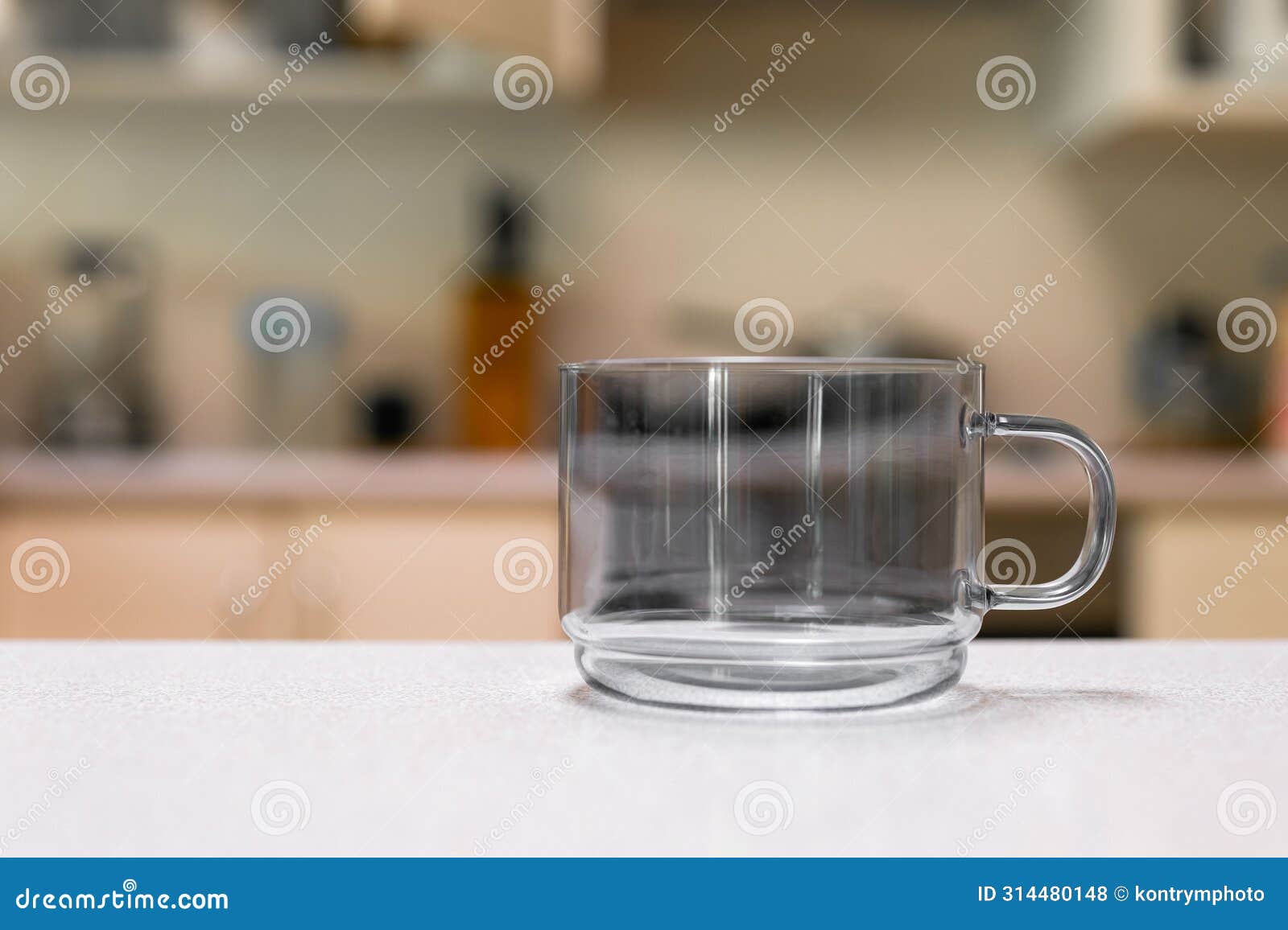 empty glass cup sitting on laminated kitchen benchtop, cupboards and cooking appliances in background