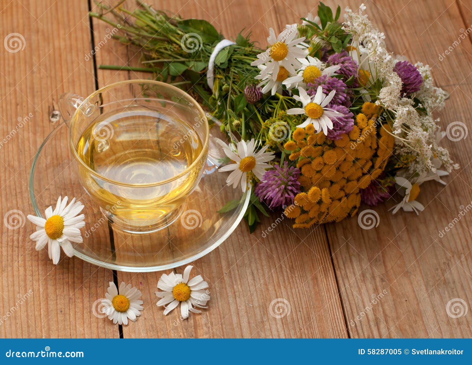 En kopp av kamomillte i en glass kopp och en bukett av fältsommar blommar på en träyttersida - nära övre