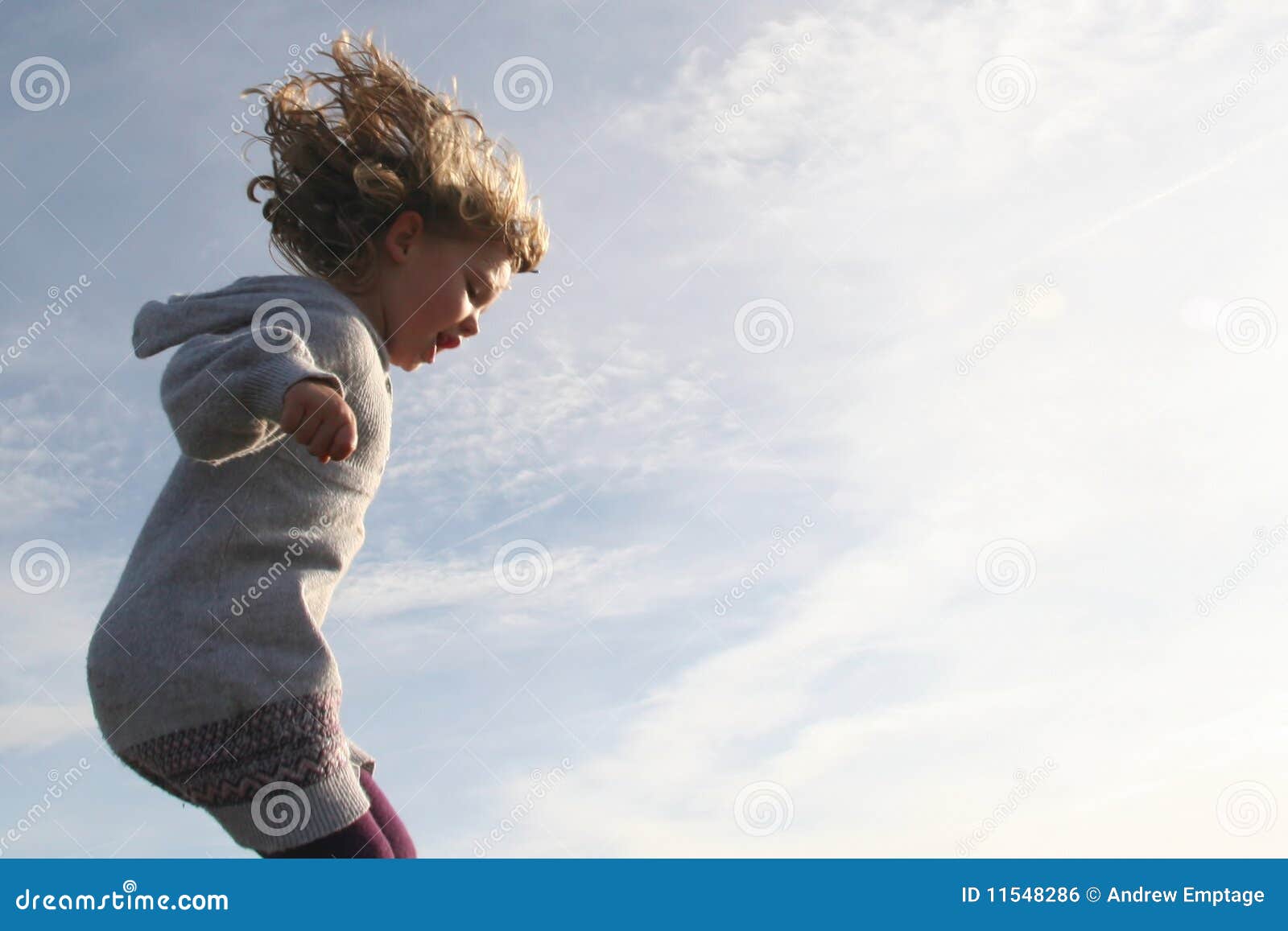 En meisje dat loopt springt. Jong meisje dat met golvend haar in de wind op een zonnige dag bij het strand springt. Rechterkant van beeld geblazen witte en verlaten spatie voor exemplaar