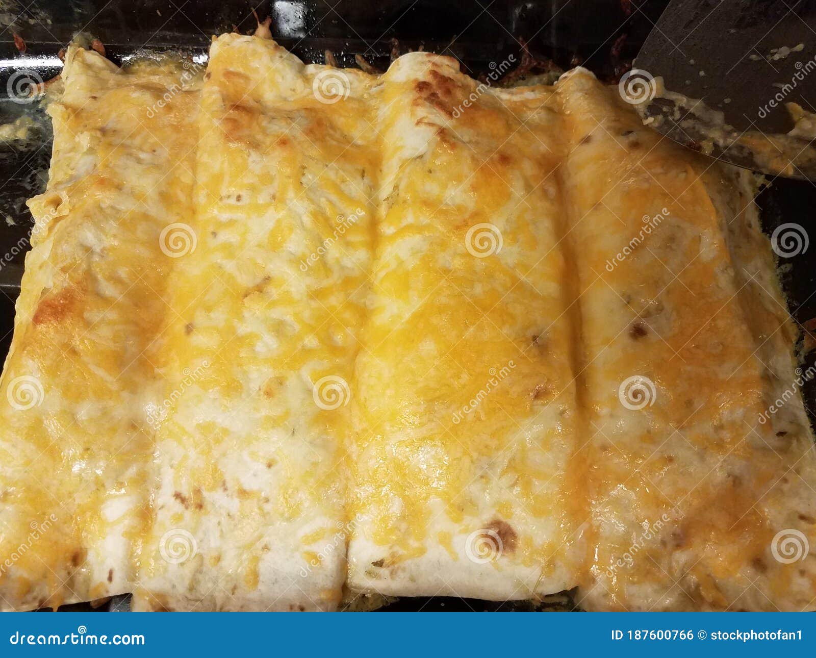 Enchiladas with Cheese in Glass Pan on Stove with Spatula Stock Photo