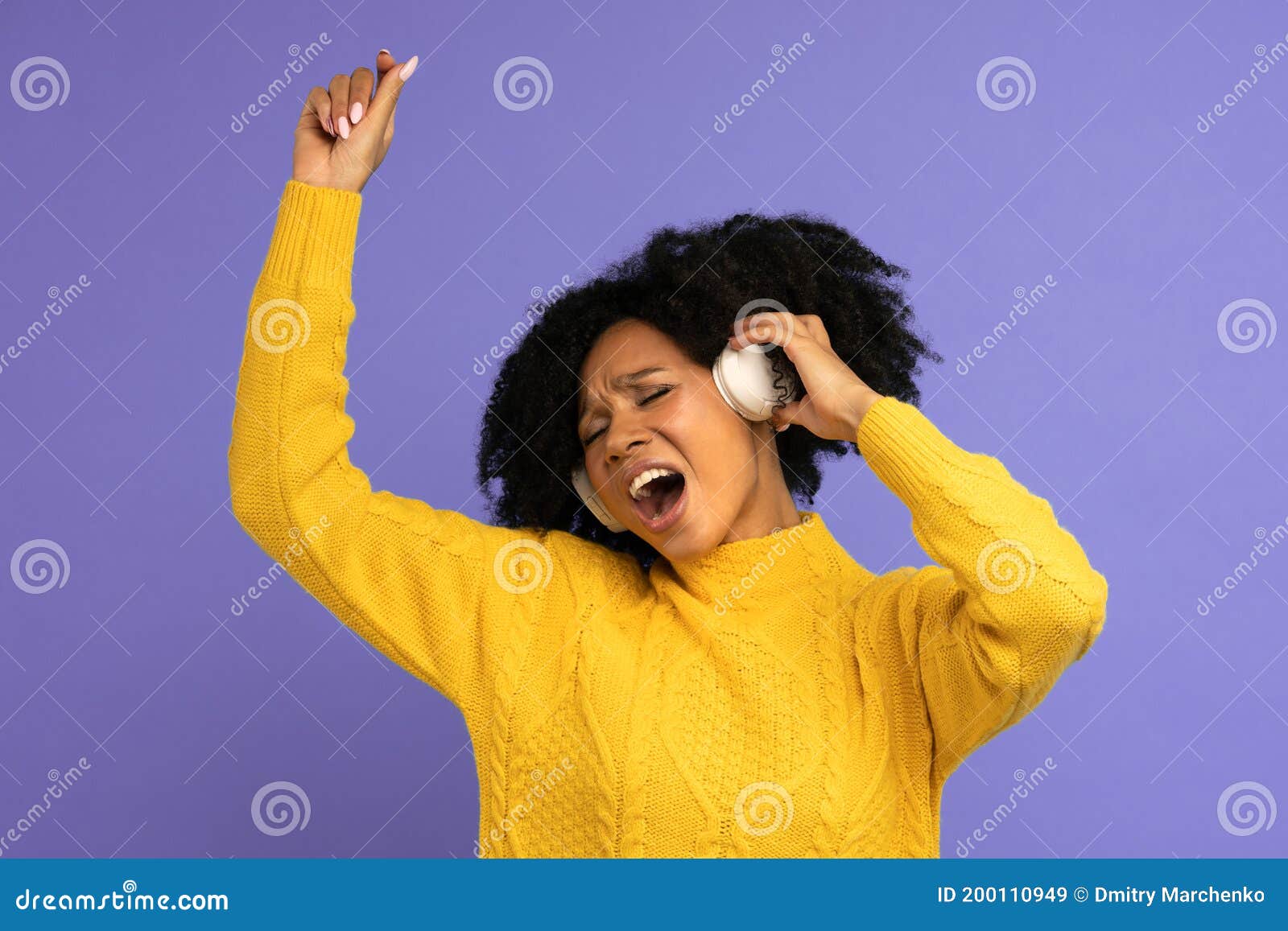 energized biracial woman sing along, wears wireless headphones, has good mood,  on violet background. happy dark skinned