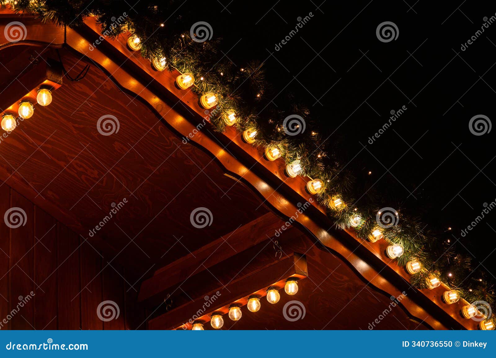 energy saving glowing string led lights hanging under a wooden roof with festive green garland. rustic holiday decor, enhancing