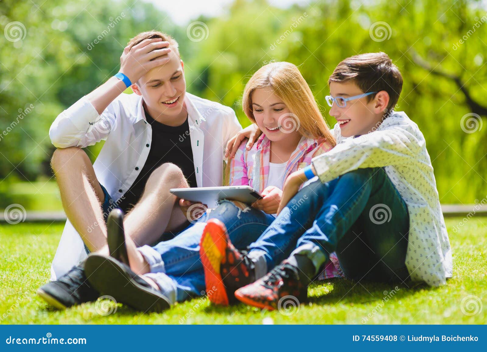 Enfants de sourire ayant l'amusement et le regard à marquer sur tablette à l'herbe Enfants jouant dehors en été les adolescents c. Enfants de sourire ayant l'amusement et le regard au comprimé à l'herbe Enfants jouant dehors en été les adolescents communiquent extérieur