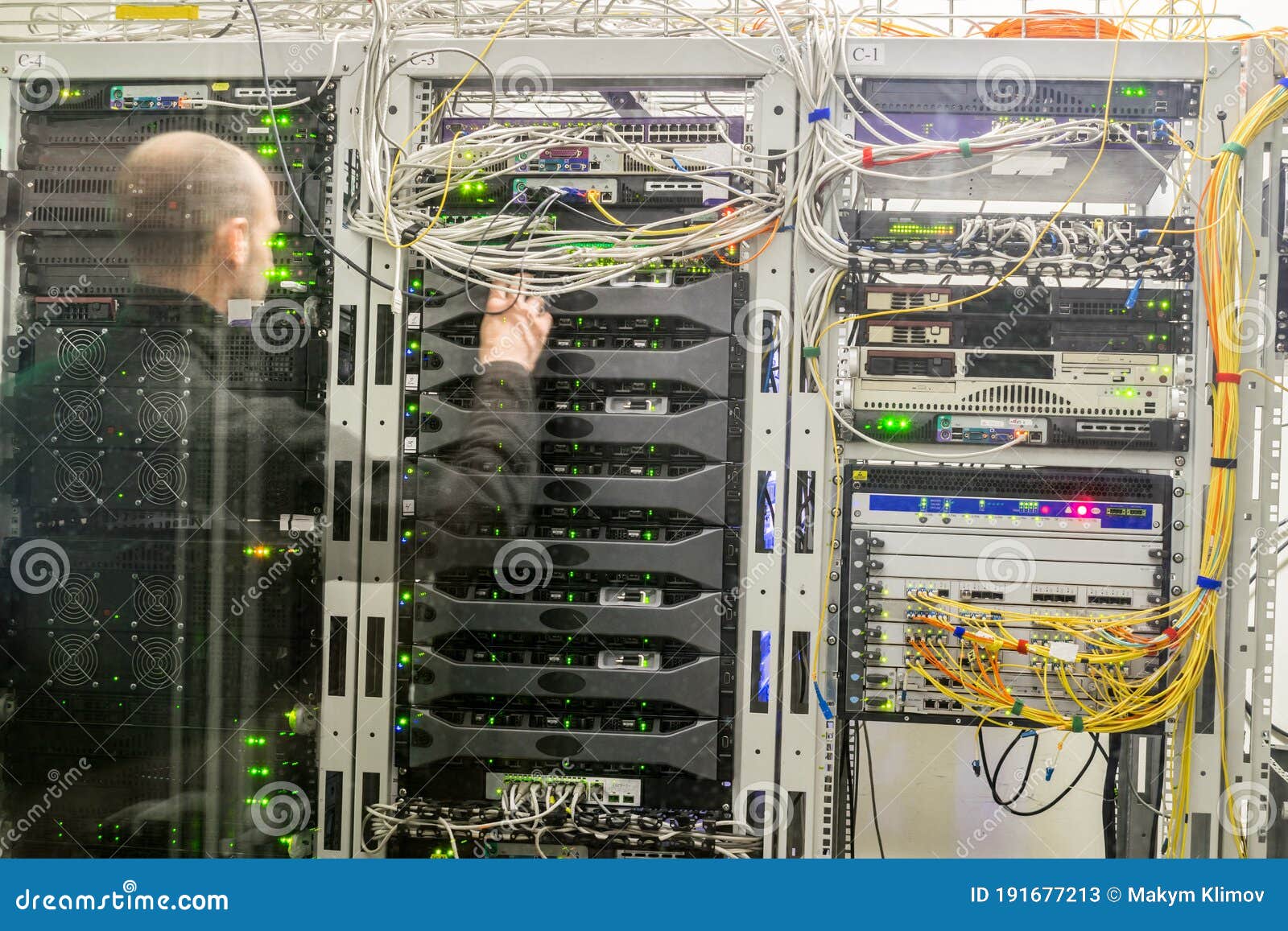 The Engineer Works in the Server Room. a Man is Behind a Glass