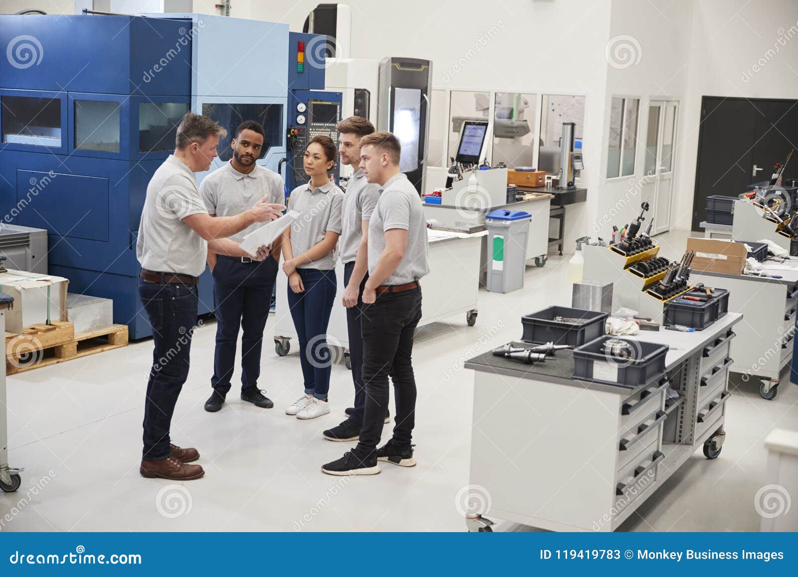 engineering team meeting on factory floor of busy workshop