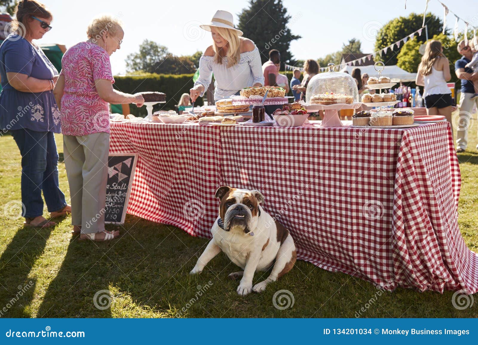 english bulldog sitting by cake stall at busy summer garden fete