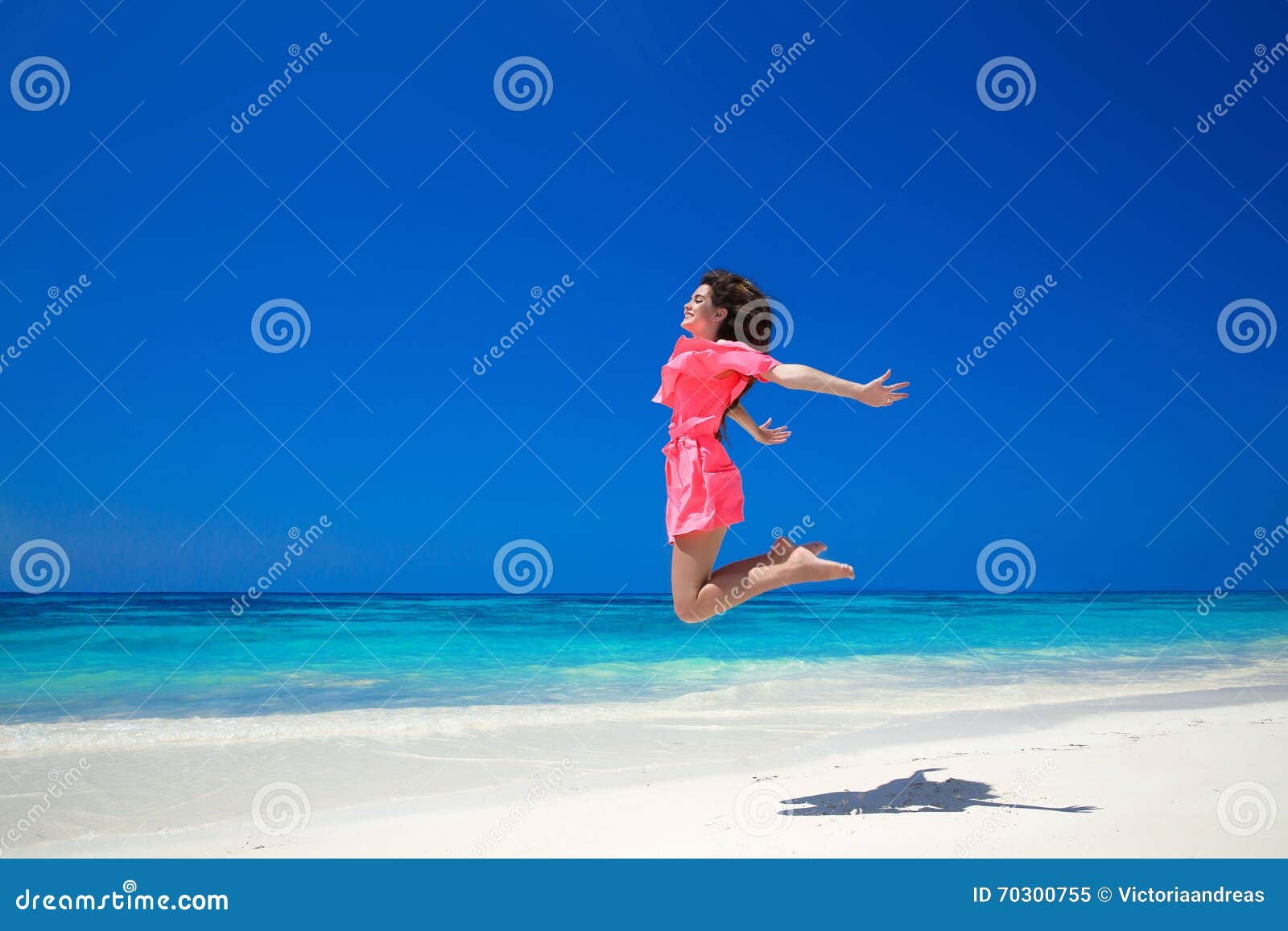 enjoyment. happy free woman jumping over sea and blue sky, brunette smiling girl in red dress on tropical beach. enjoyment.