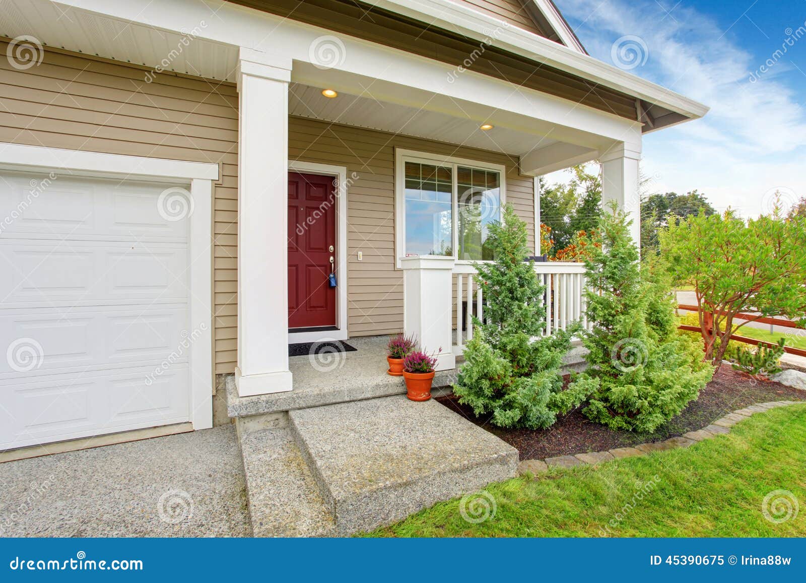 Entrance porch with front yard landscape. Entrance porch with railings and red door. Front yard landscape with decorative fir trees