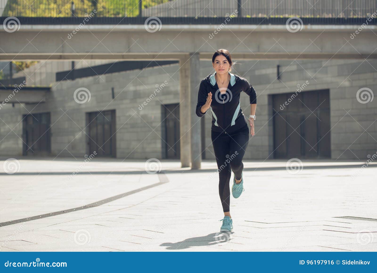 Entrenamiento del ejercicio activo de la mujer joven en la calle al aire libre. Entrenamiento femenino joven del ejercicio activo en el funcionamiento exterior de la calle