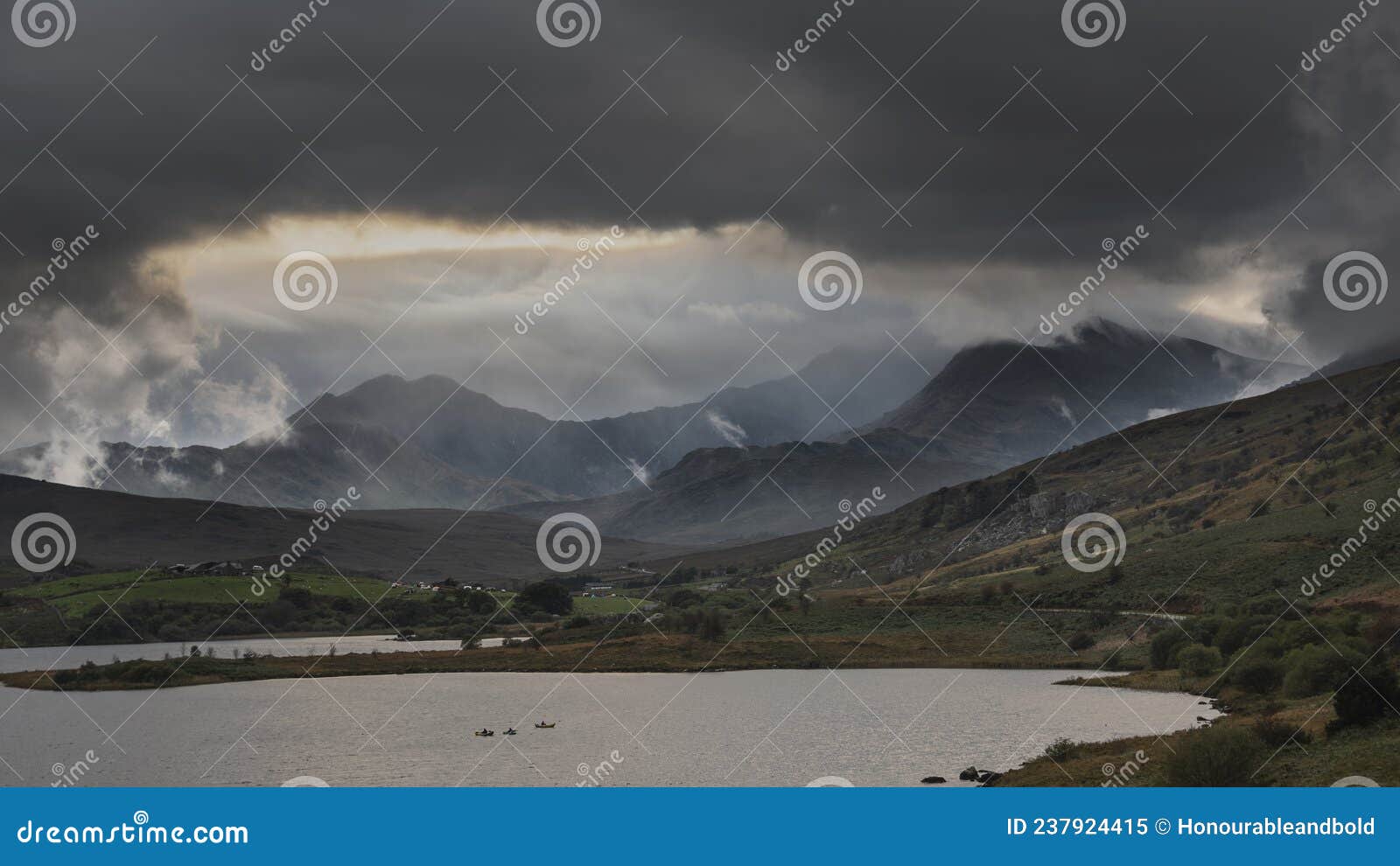 epic stunning autumn landscape image of snowdon massif viewed from shores of llynnau mymbyr at sunset with dramatic dark sky and