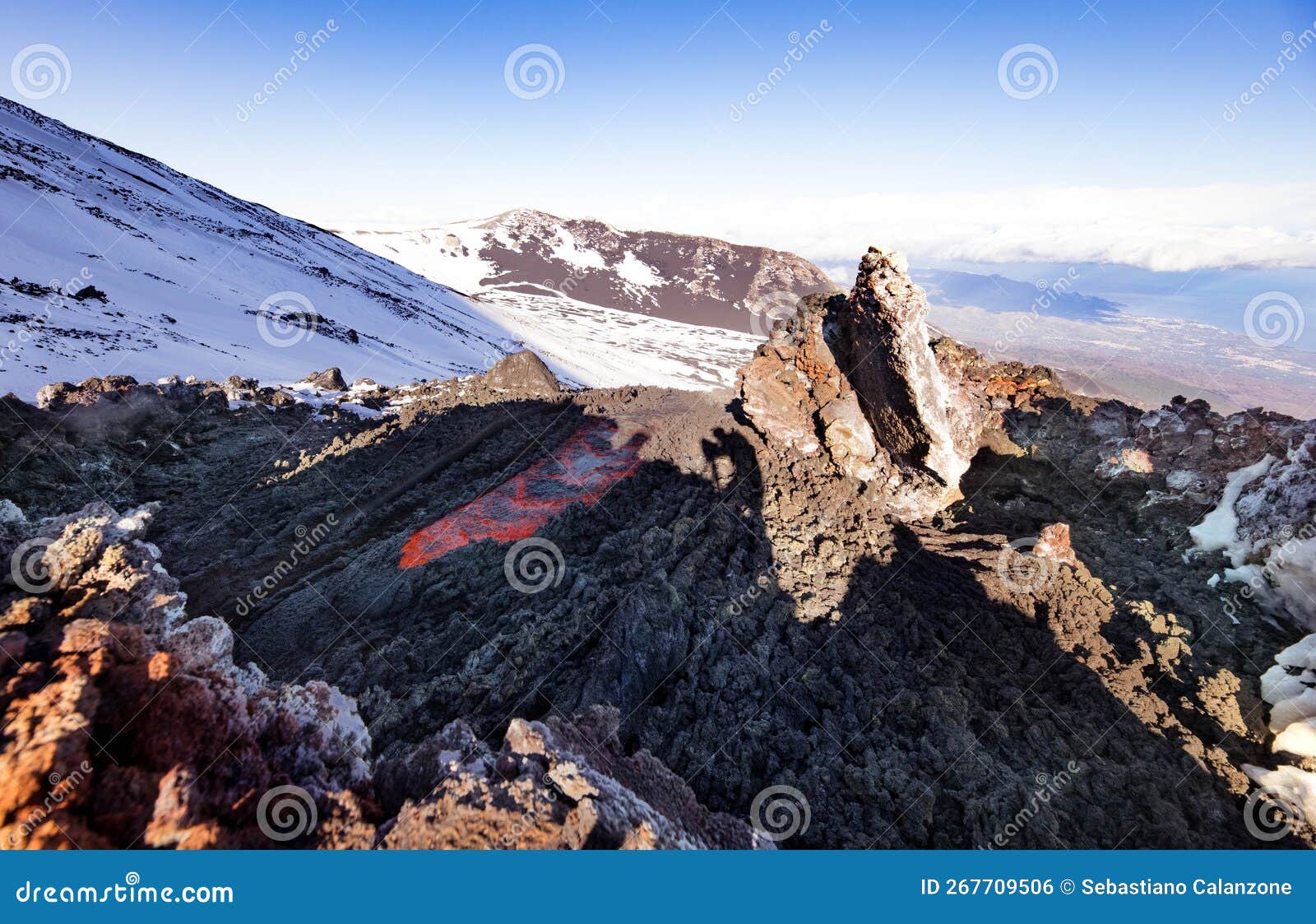 eruzione sull etna con colata di lava al tramonto nel paesaggio invernale con cielo blu