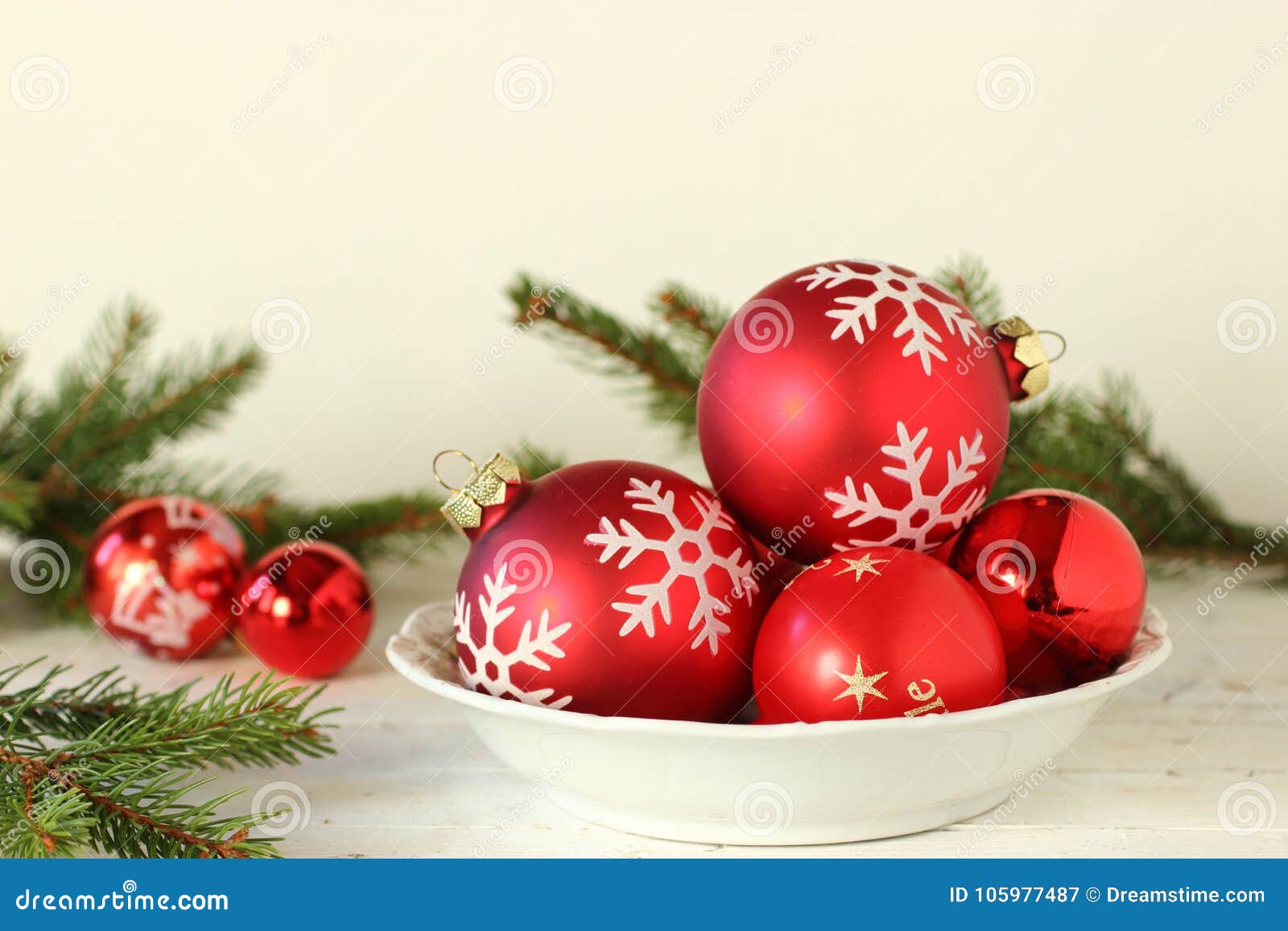 Esfera vermelha do Natal no fundo branco. Uma bacia de bola vermelha do Natal na tabela com ramos verdes