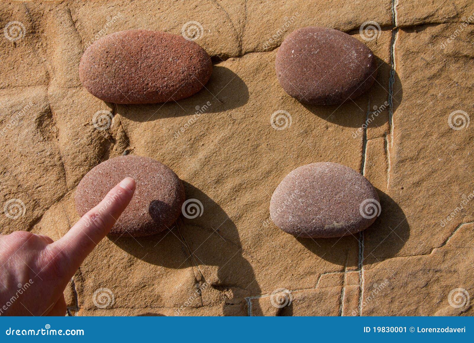 Estale sobre uma pedra 02. Uma mão que indica uma pedra em um quadrado de quatro pedras redondas sobre uma rocha