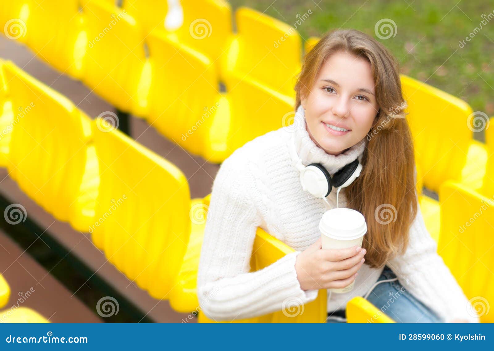 Estudante fêmea novo que tem o resto exterior. Relaxamento feliz bonito do estudante exterior. Menina de sorriso bonita que tem a ruptura com café e livro em seus joelhos que sentam-se na fileira de assentos plásticos amarelos no estádio da escola. Resto do estudo.