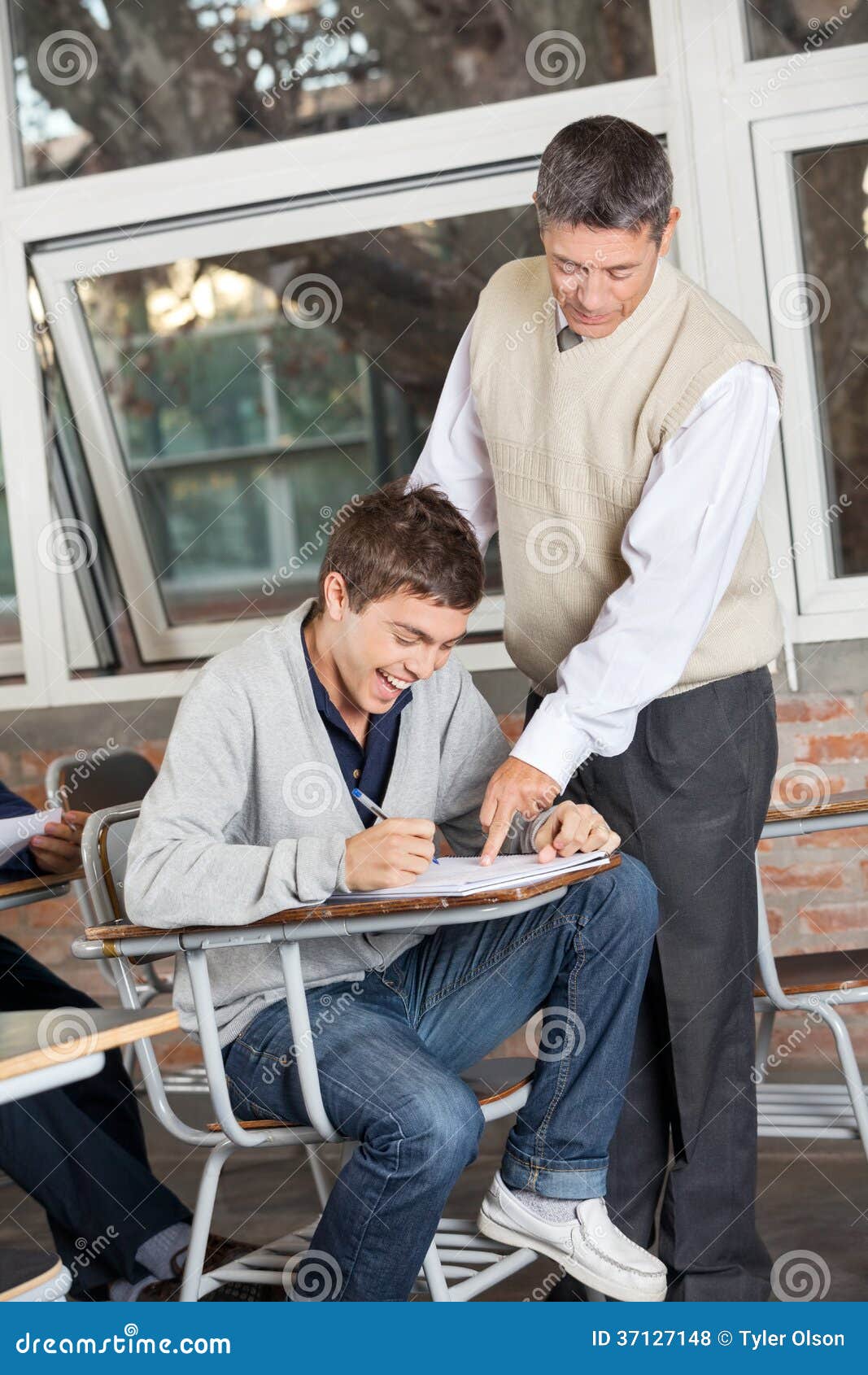 Estudante Smiling While Teacher que explica o teste dentro. Estudante universitário nova que sorri quando professor que explica o teste na sala de aula