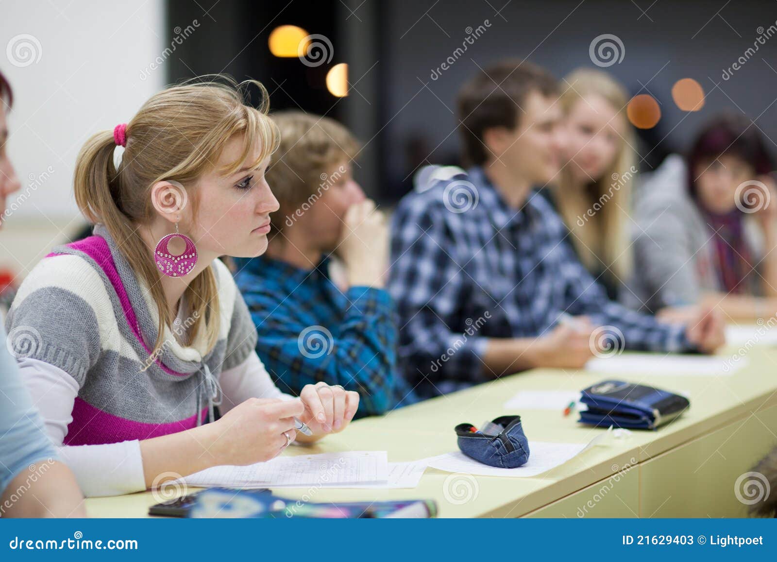 Estudiante universitario de sexo femenino bonito en una sala de clase. Estudiante universitario de sexo femenino bonito que se sienta en una sala de clase por completo de estudiantes durante la clase (DOF bajo; imagen entonada color)