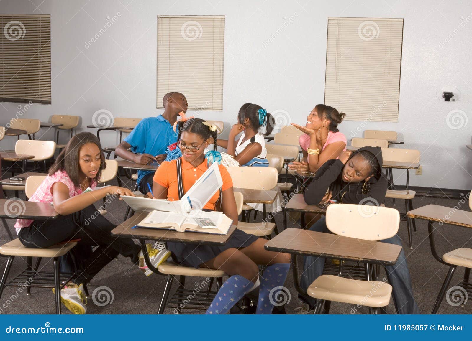 Estudiantes de Highschool que ensucian en clase durante rotura. Sala de clase de la High School secundaria con seis niños, un muchacho y cinco muchachas, haciendo caos