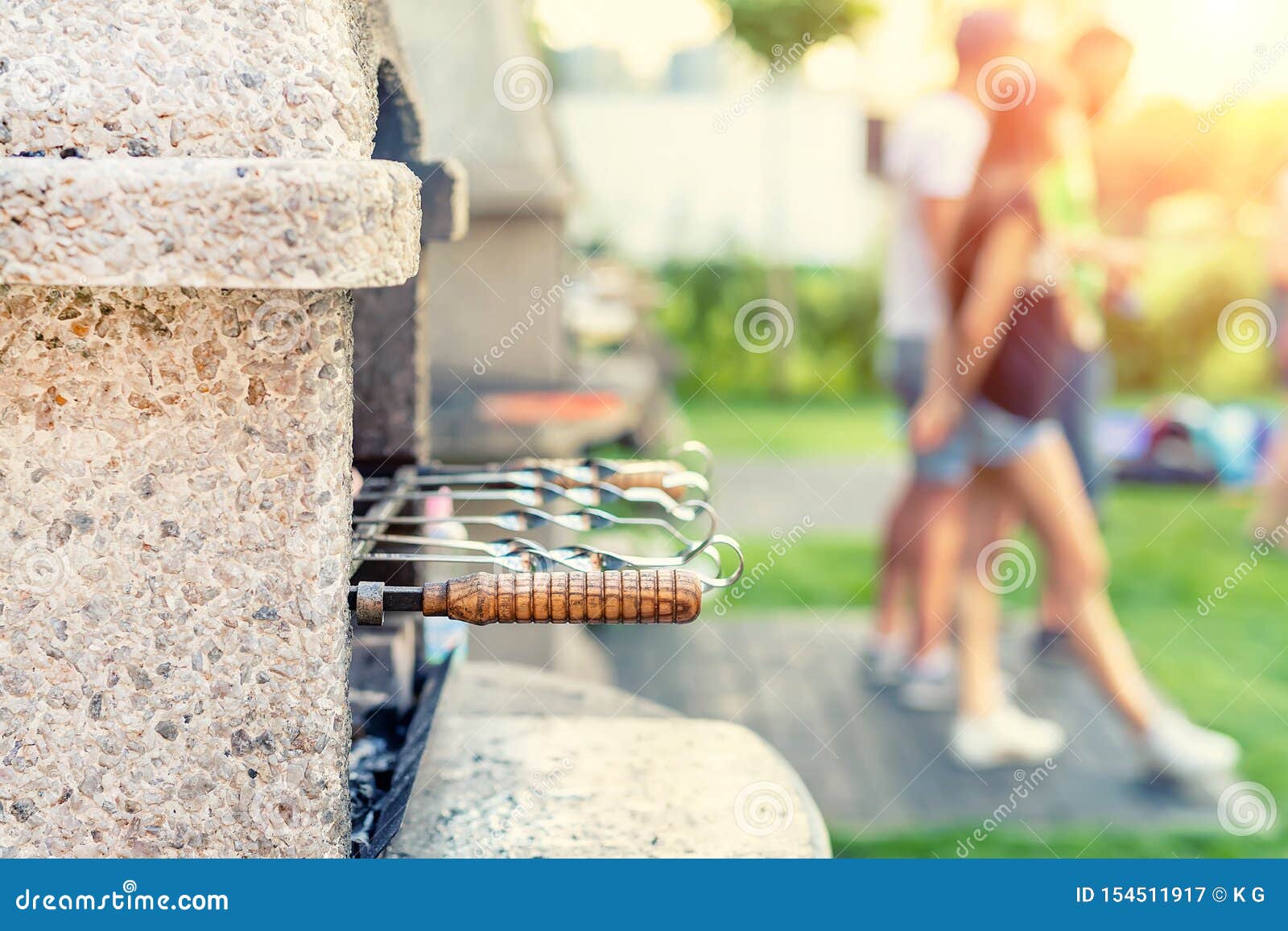 Estufa de piedra al aire libre con la parrilla y los pinchos Compañía de amigos en el partido de la barbacoa en el parque o el patio trasero con el césped y el brasero de la hierba verde Gente que se divierte que cocina la comida durante fin de semana del Bbq en el jardín, sove, horno, verano, comida, carne, feliz, forma de vida, naturaleza, grupo, junto, asado a la parilla joven, barbacoa, fondo, comiendo, cena, almuerzo, caucásico, comida campestre, hogar, familia, fuego, mujeres, asado a la parrilla, masculinas, hembra, vacaciones, calientes, día de fiesta, amistad, humo