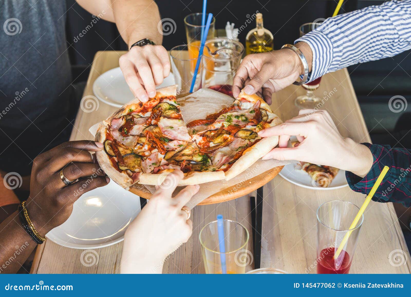 A company of multicultural young people in a cafe eating pizza, drinking cocktails, having fun.