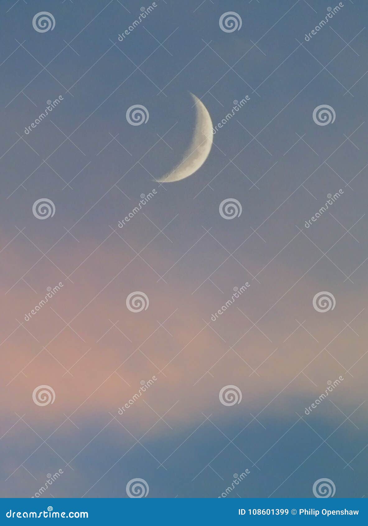 crescent moon in a blue sky with pale pink clouds