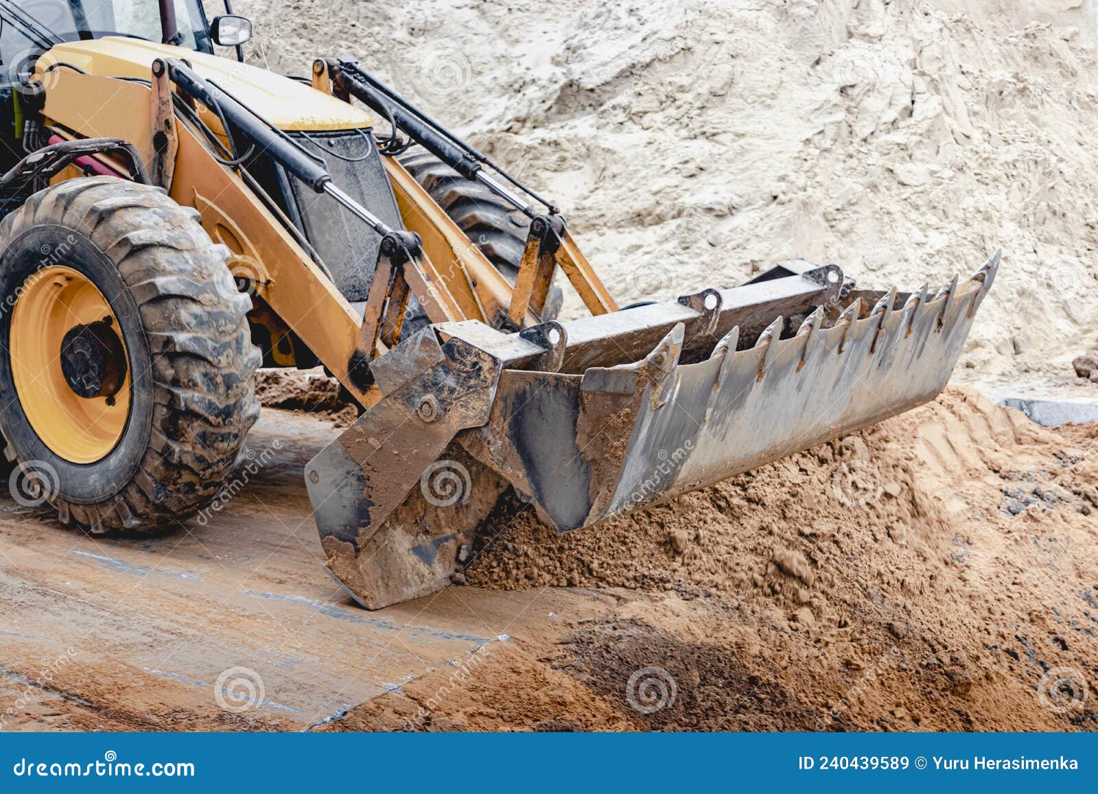 the excavator backfills the pit with the front bucket. moves soil around the construction site. close-up. heavy construction