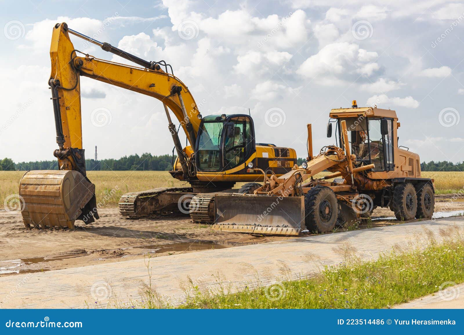 The Excavator and the Grader Stand Side by Side Against the Blue Sky. Heavy Construction