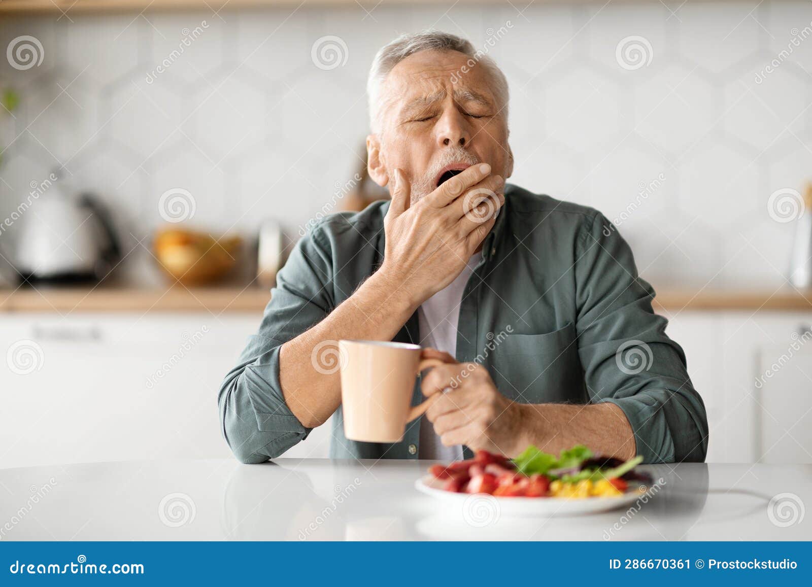 excessive daytime sleepiness. tired senior man yawning at table in kitchen