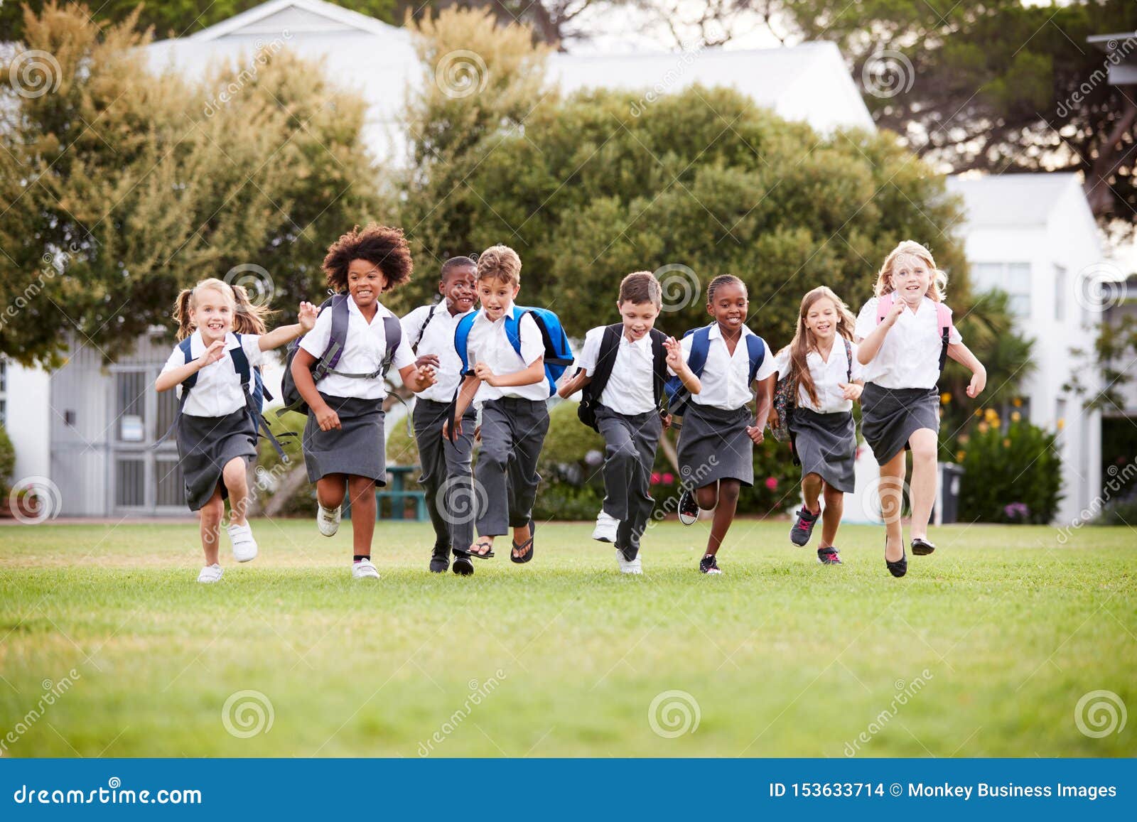 excited ary school pupils wearing uniform running across field at break time