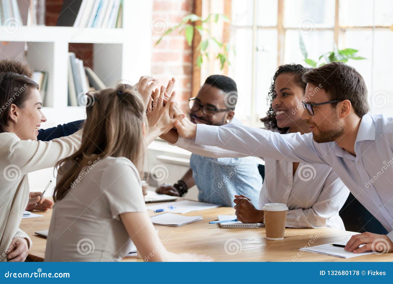 excited multiracial team giving high five at company meeting