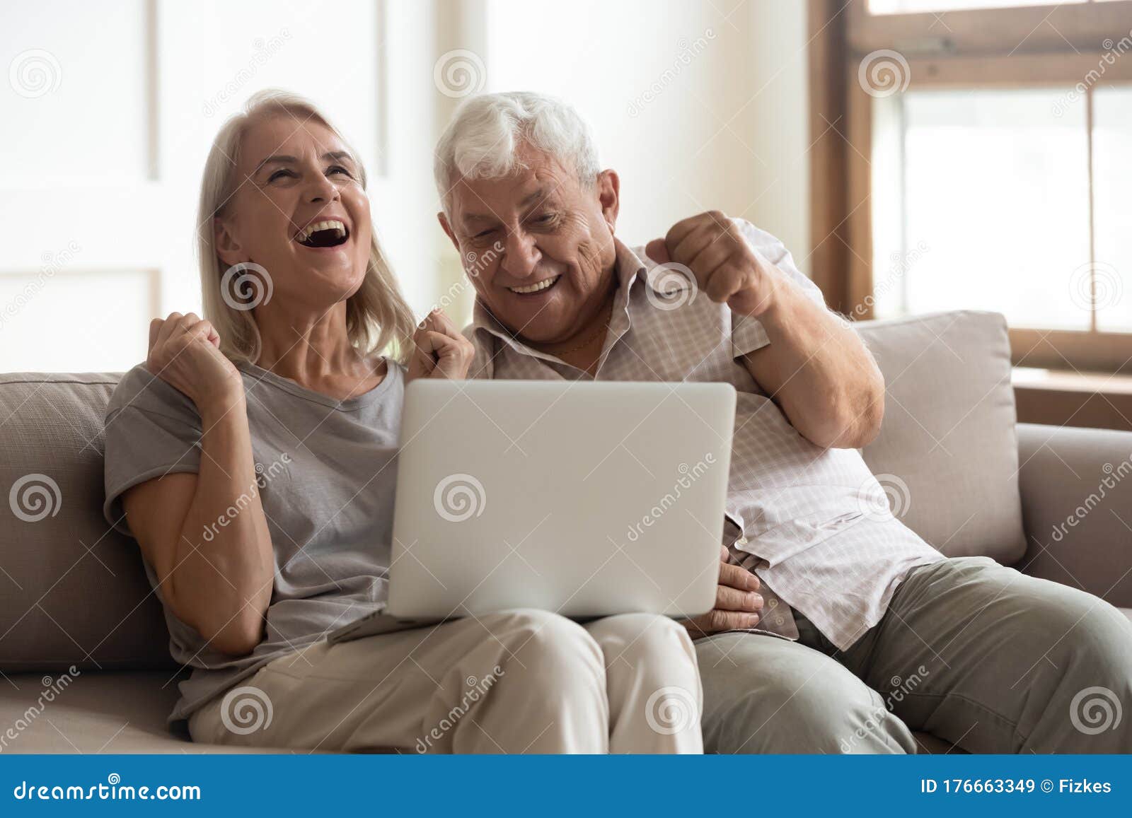 excited older wife and husband celebrating online win, using laptop