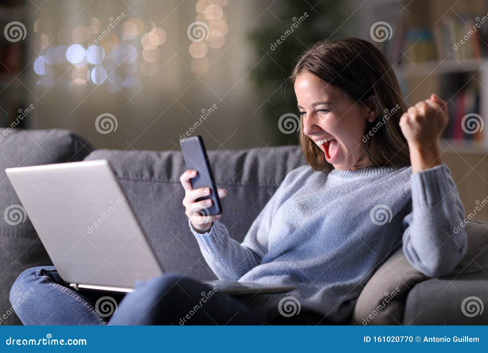 excited woman using phone and laptop in the night