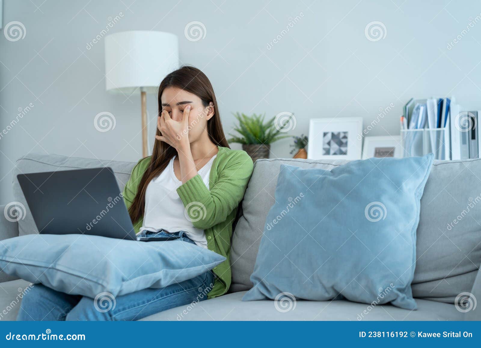 exhausted asian business woman hurt eye while using laptop computer. young girl office worker sit on sofa feel visual fatigue and