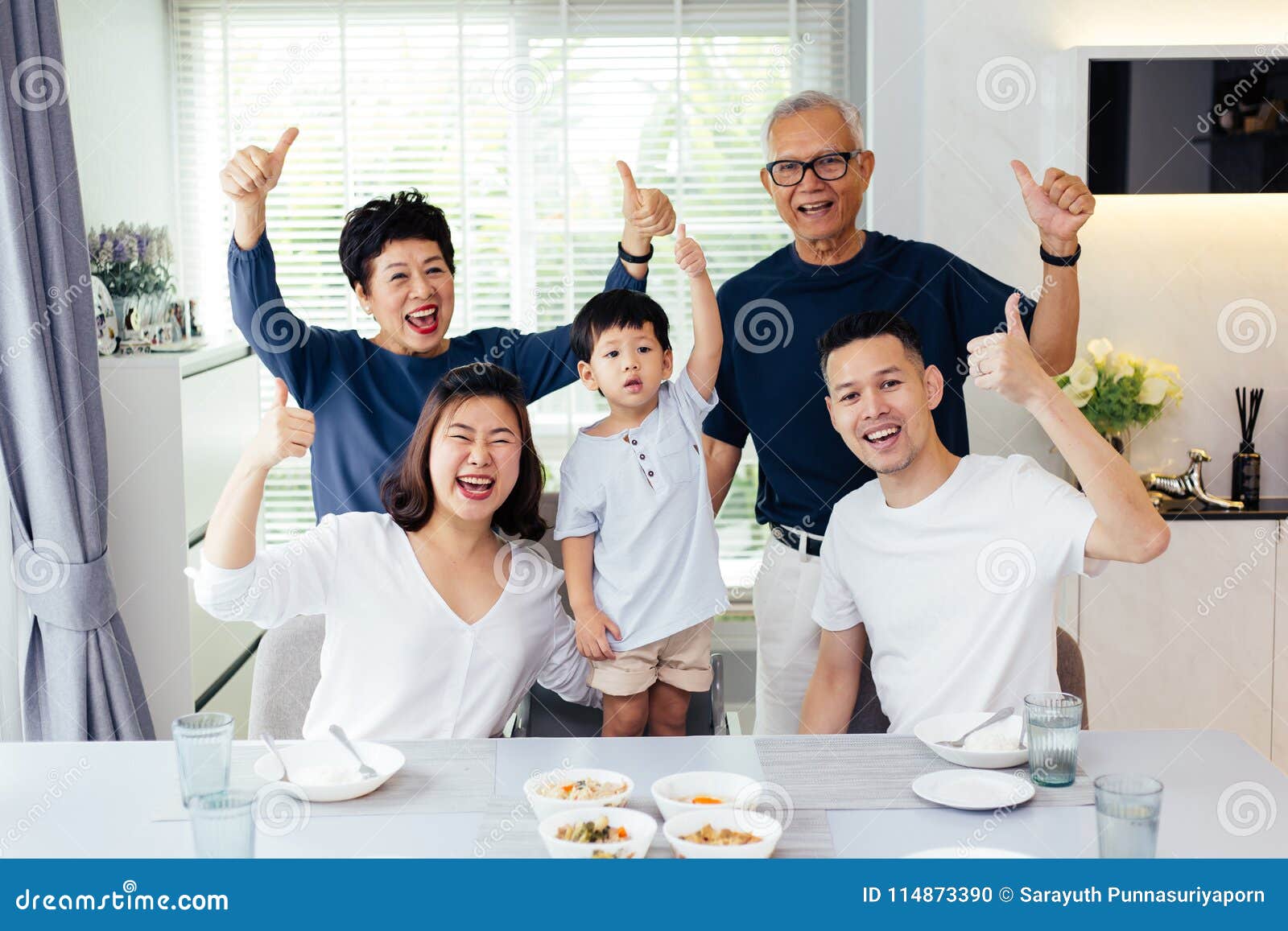 extended asian family of three generations having a meal together and showing thumbs up at home with happiness