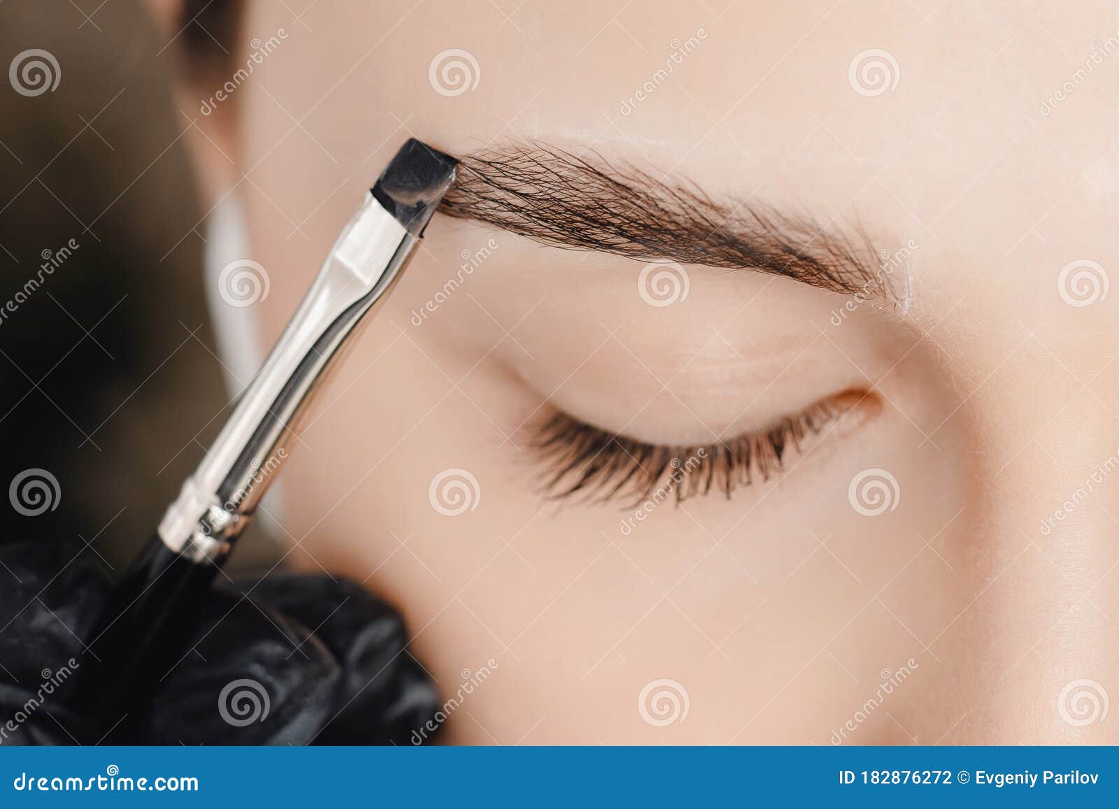 correction and tint of eyebrows, master applies brush to woman marking on brow