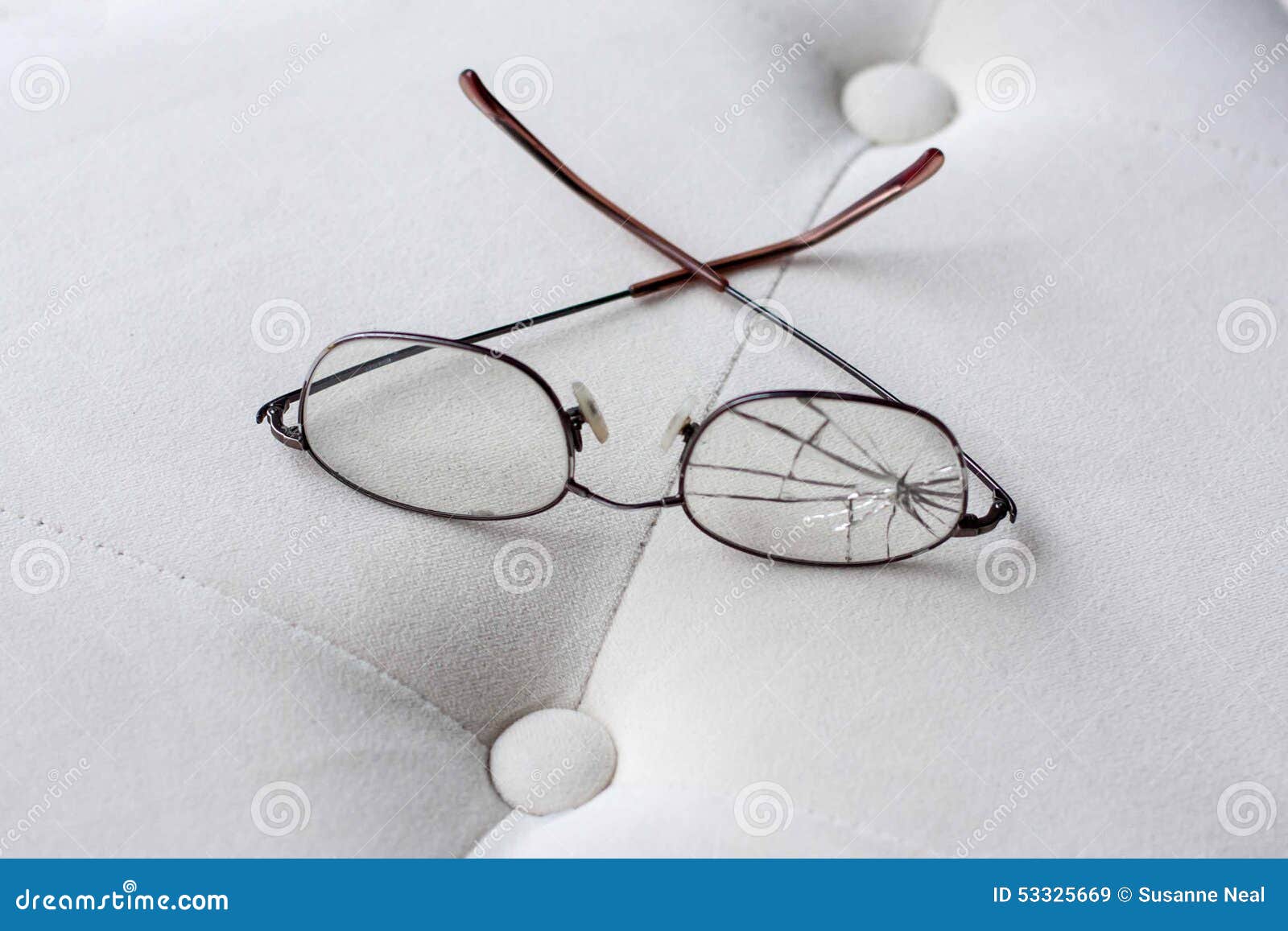 eyeglasses with cracked lens on cream colored ottoman