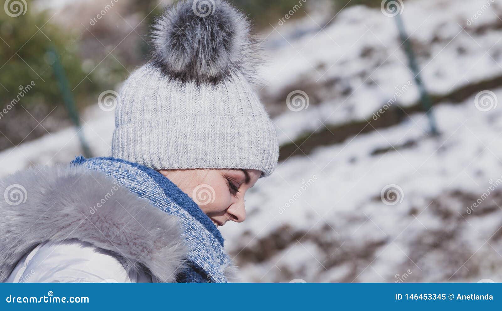 F?mea que veste o equipamento morno durante o inverno. Pretty young woman wearing warm accessories during winter time. Female having grey beanie warm hat with pompons and blue scarf