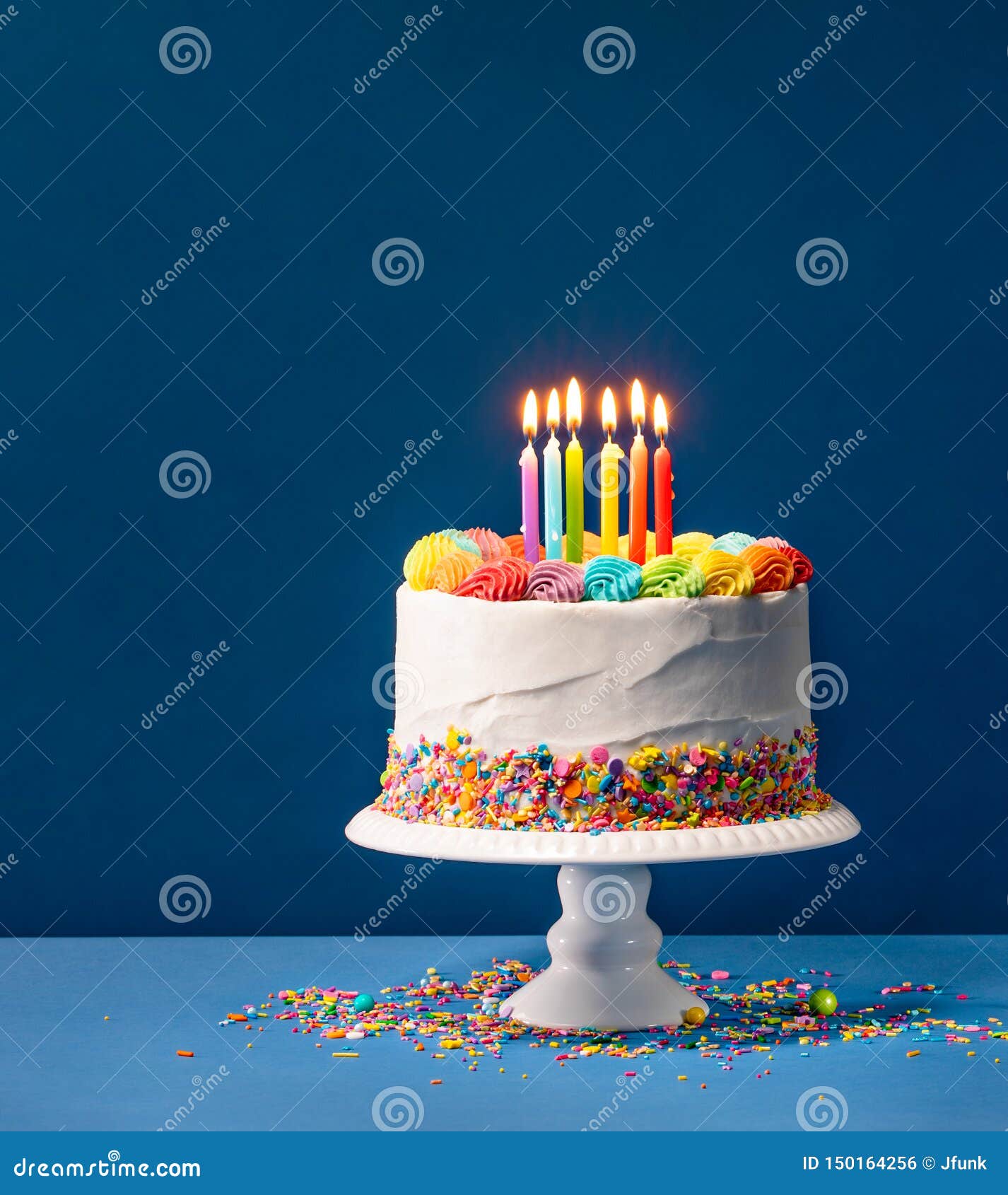 Colorful Birthday Cake over Blue. Birthday cake with rainbow icing, colorful Sprinkles and lit candles over a blue background