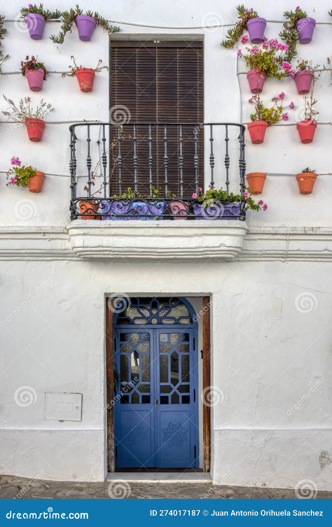 traditional andalusian village facade decorated with pots, with blue wooden door and balcony, in vejer de la frontera, spain