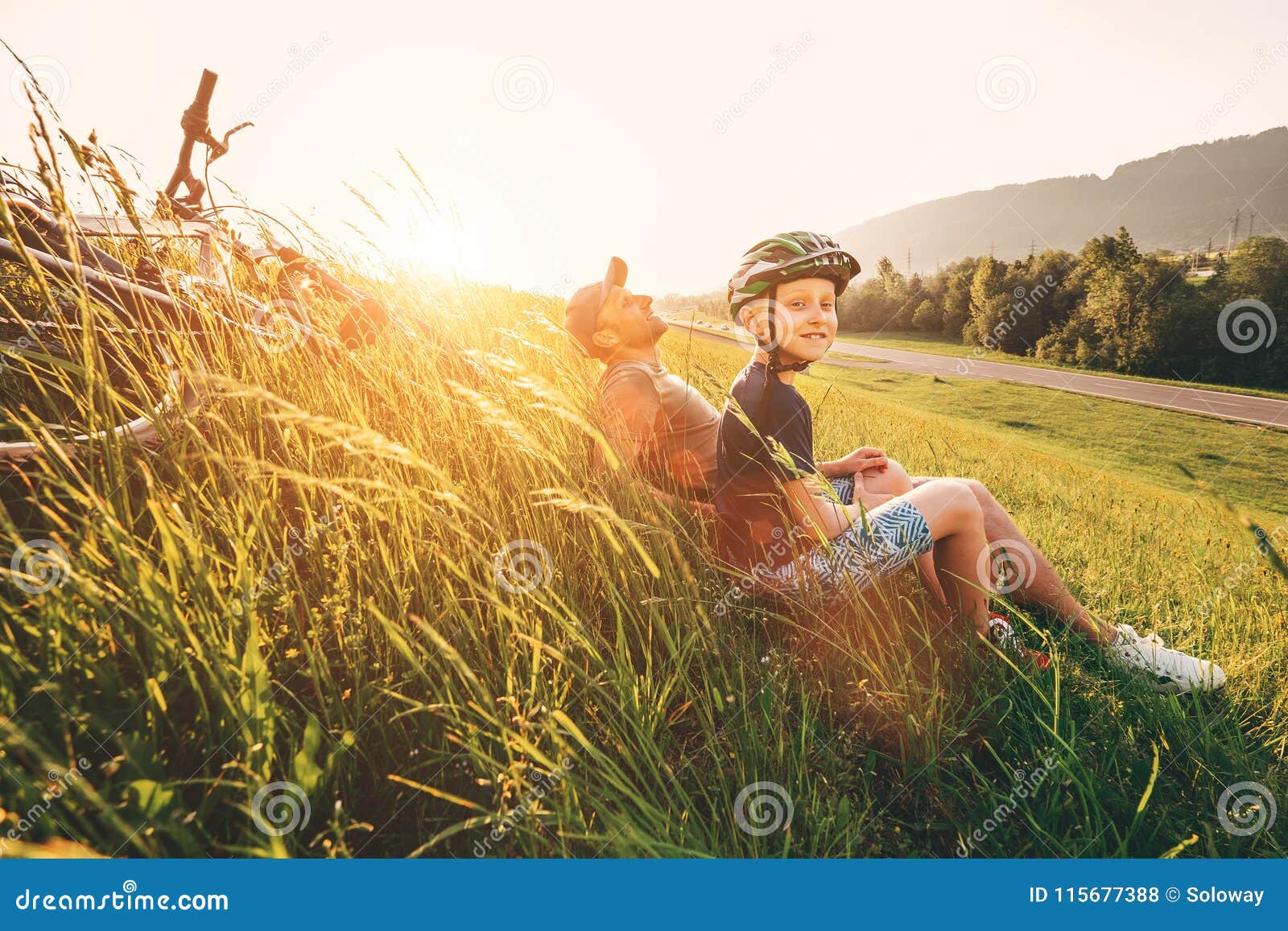 Fadern och sonen vilar i högt grönt gräs, efter cykeln har gått